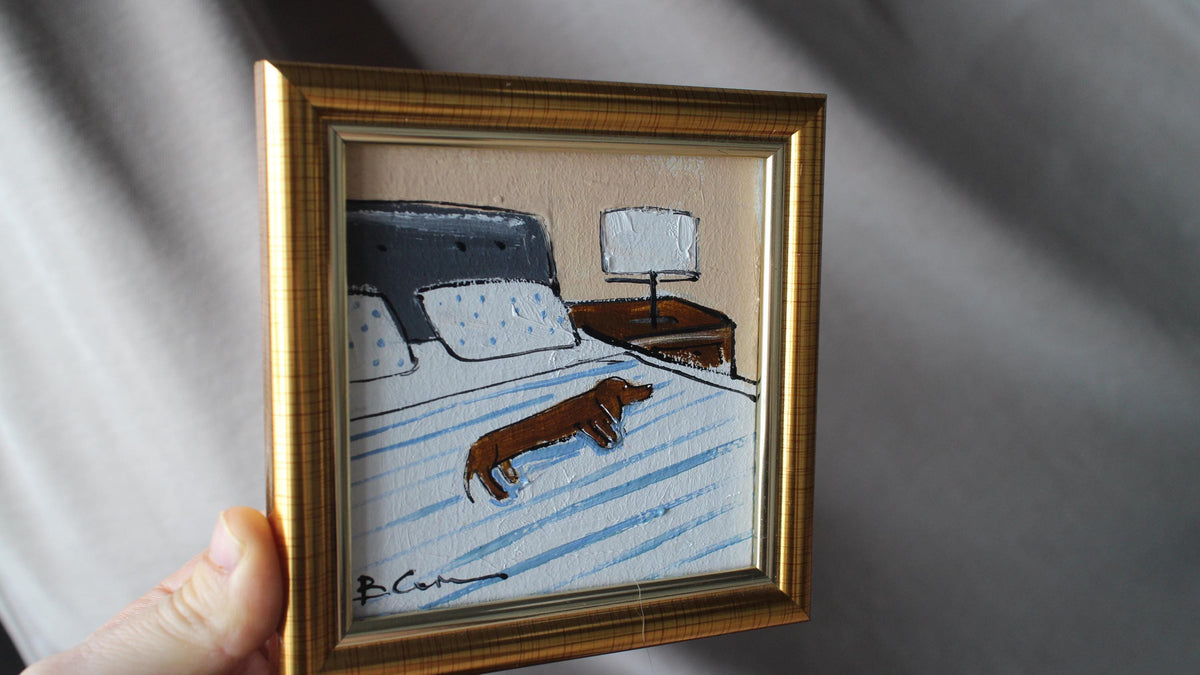 Framed artwork of a bedroom scene with a dog on a bed.