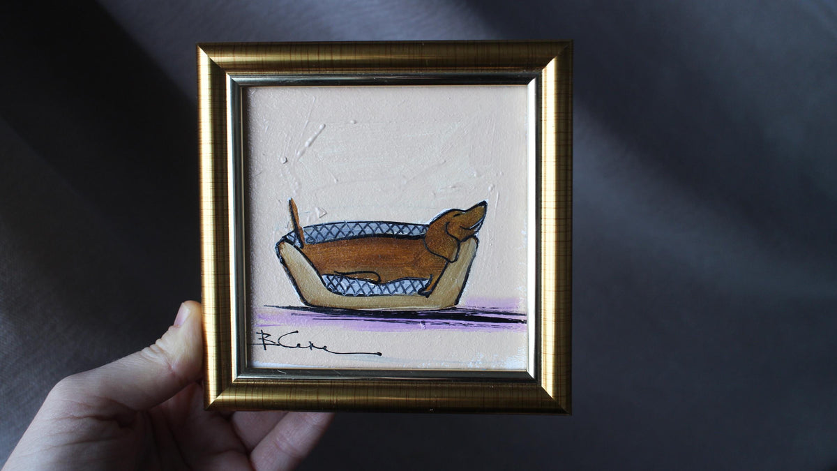 Framed artwork of a dog in a boat held by a hand against a dark background
