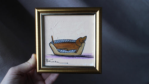 Framed artwork of a dog in a boat held by a hand against a dark background