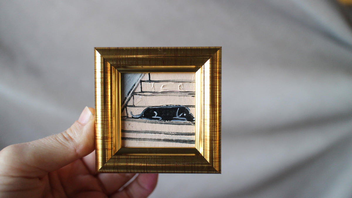 Hand holding a small gold-framed picture with a black and white image inside against a gray background