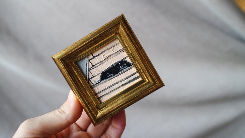 Hand holding a small gold-framed picture with a blurred background