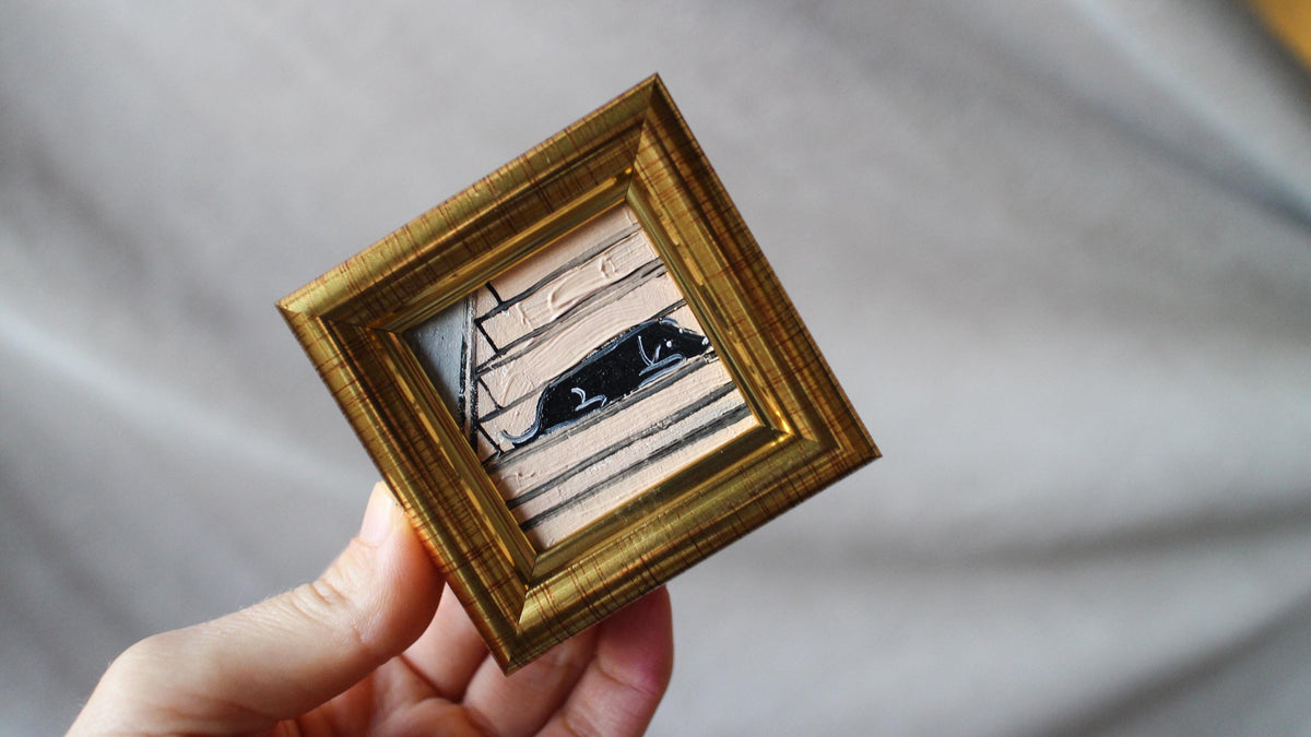 Hand holding a small gold-framed picture with a blurred background