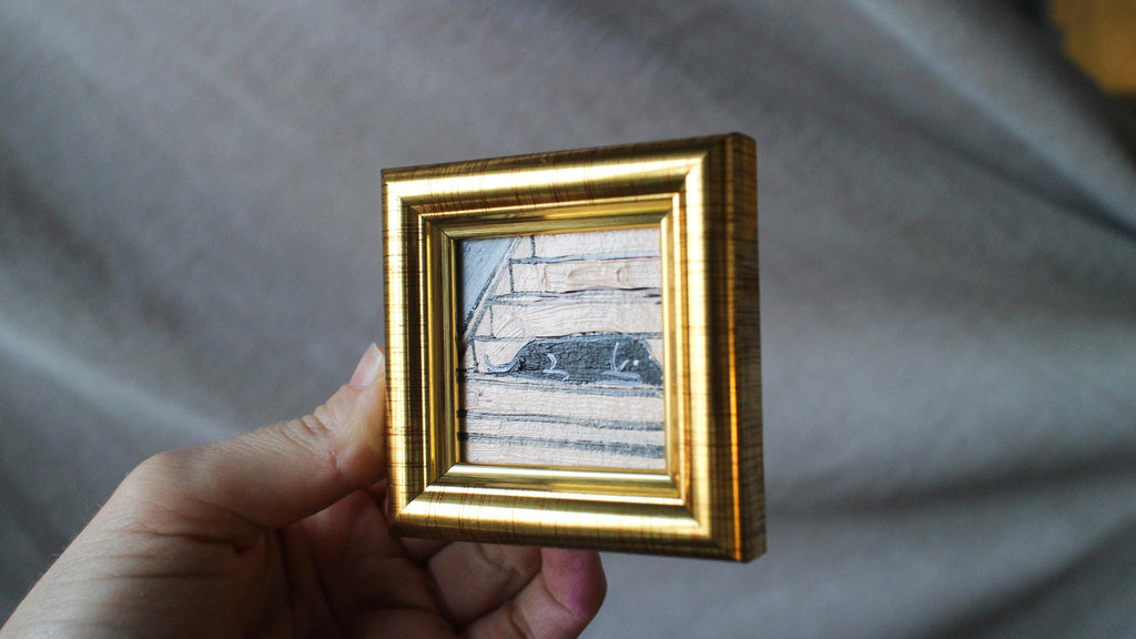 Small gold-framed picture held in a hand against a neutral background